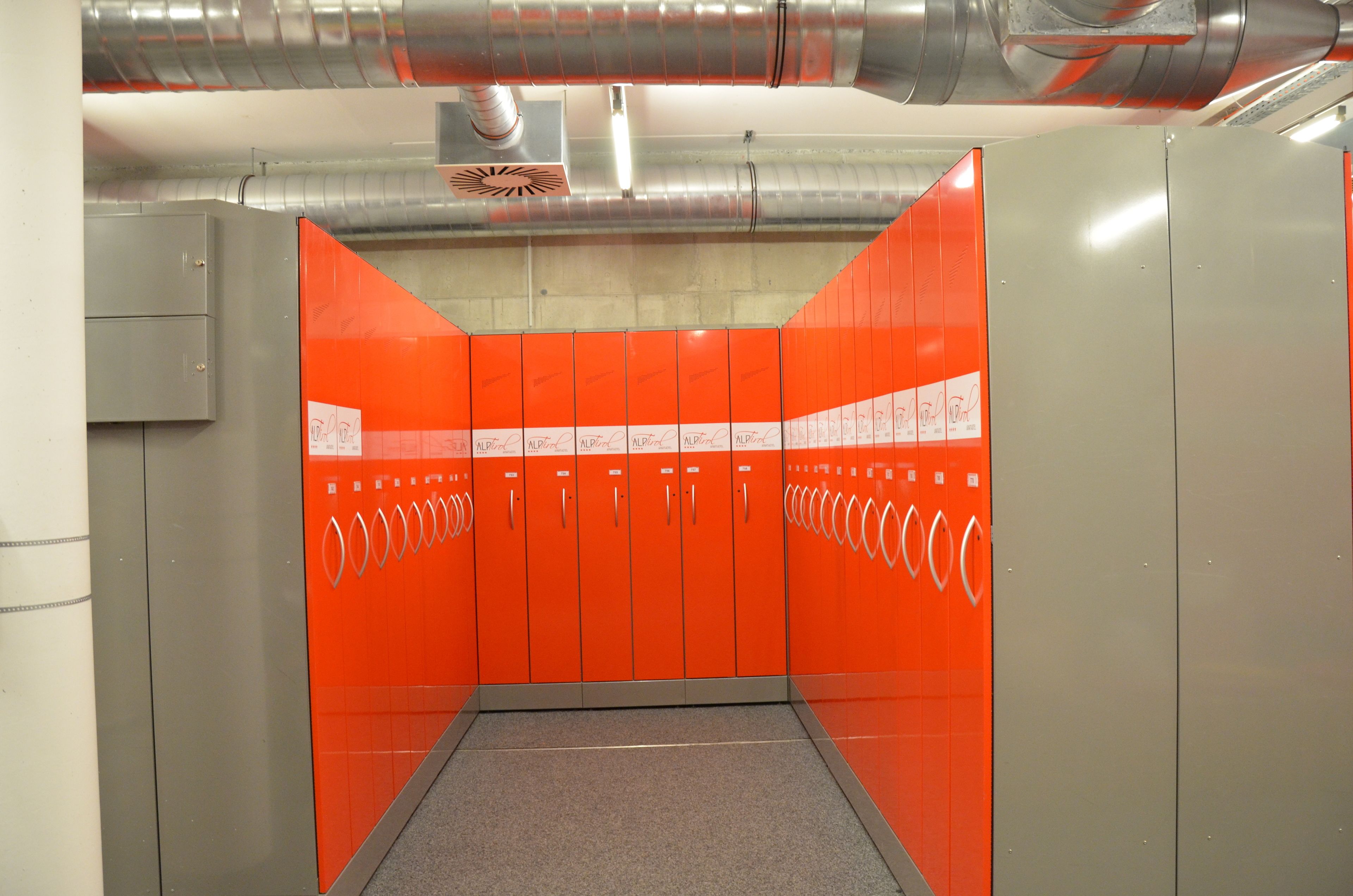 A modern elevator with orange and grey walls, featuring a series of lockers and a metallic ventilation system.