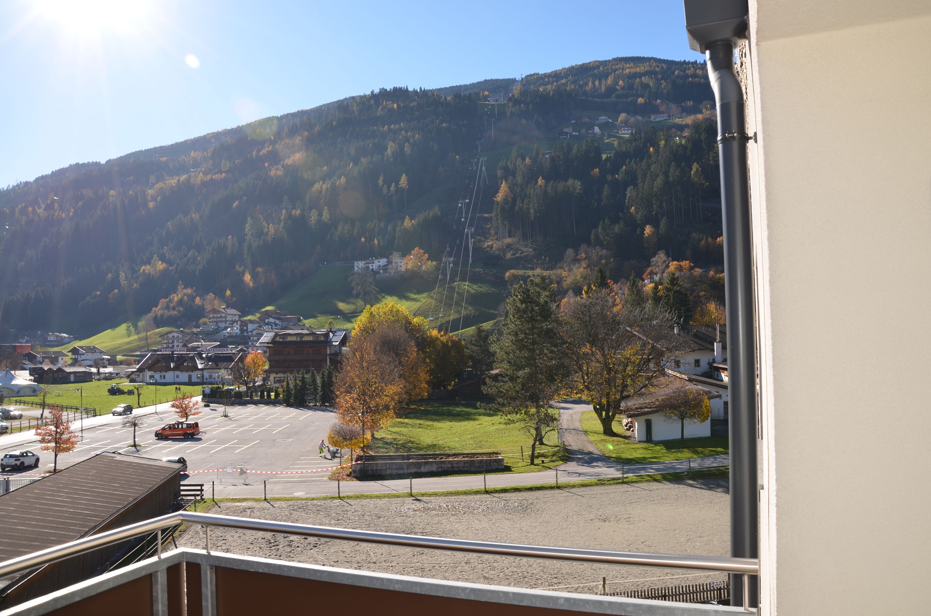 A view from a balcony overlooking a parking lot, a small building, and a hill with trees.