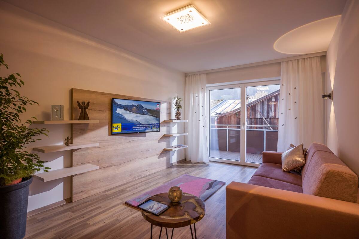 A modern living room with a wooden floor, a sofa, a coffee table, and a TV on the wall.