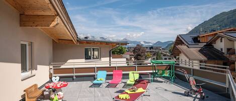 Una terrazza sul tetto con una pergola in legno, poltrone da relax colorate, una bicicletta e un passeggino.