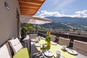 A terrace with a table set for dining, a potted plant, and a view of mountains. - Aparthotel AlpTirol (Kaltenbach)