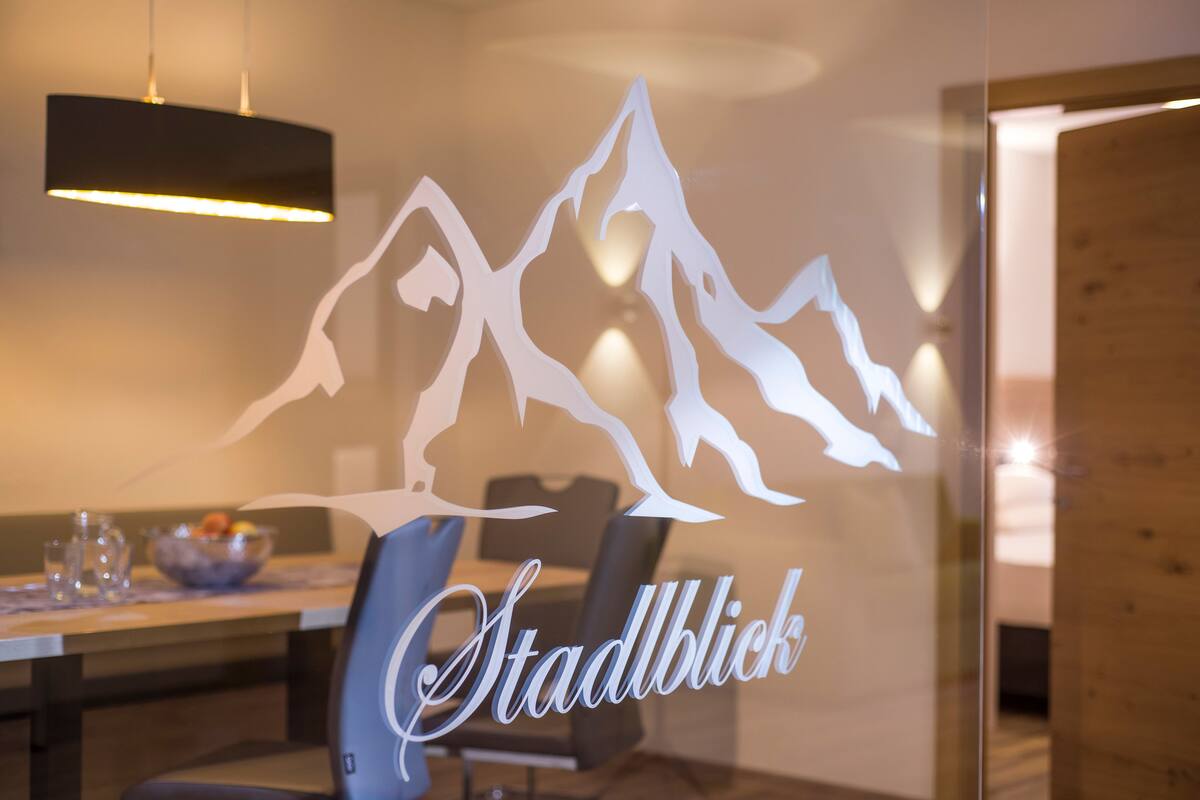 A dining area with a glass partition featuring a mountain silhouette and the word "Stadblick".