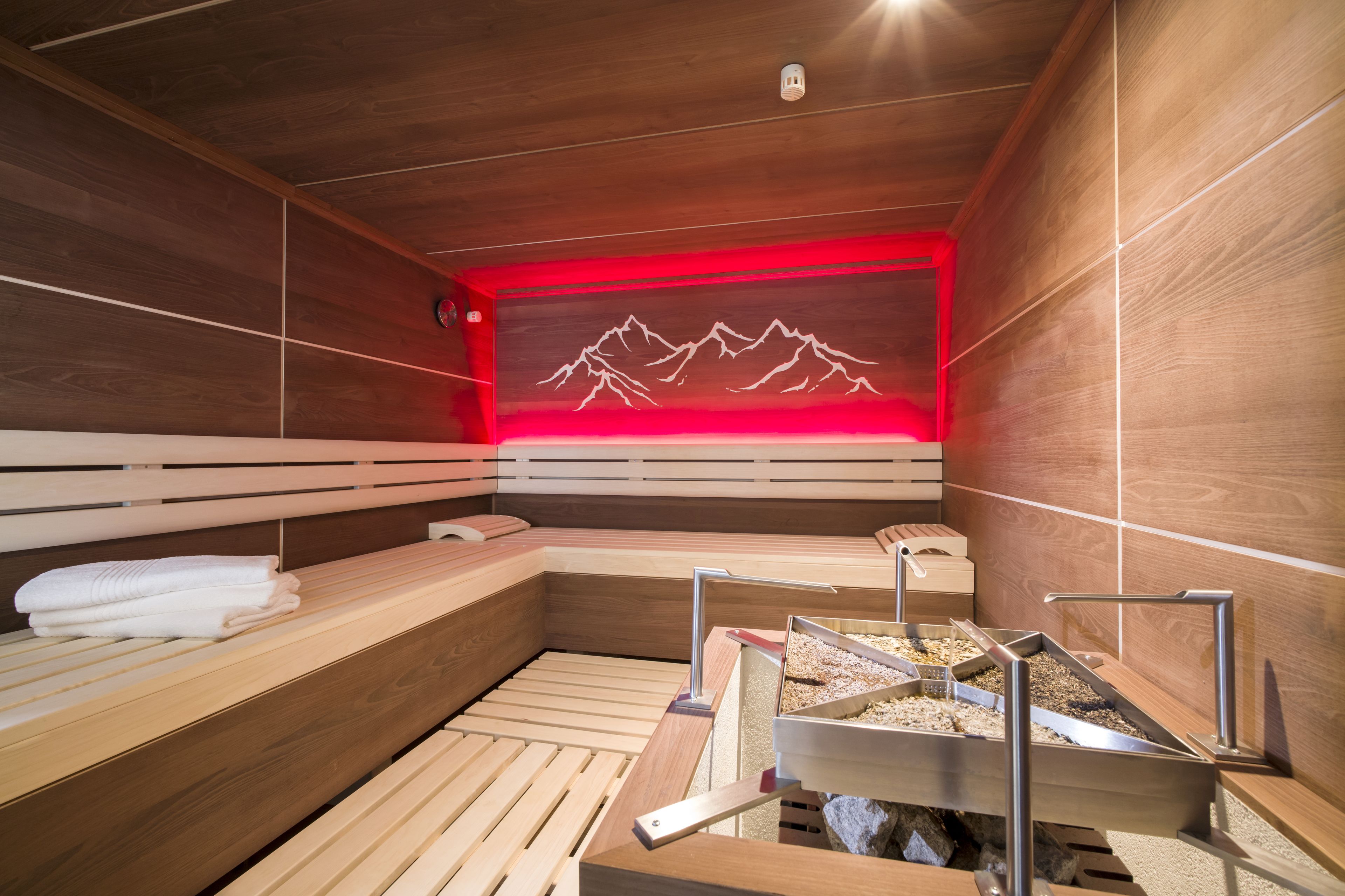 Una sala de sauna con bancos de madera, una pared iluminada en rojo y una mesa de sauna metálica con una bandeja.