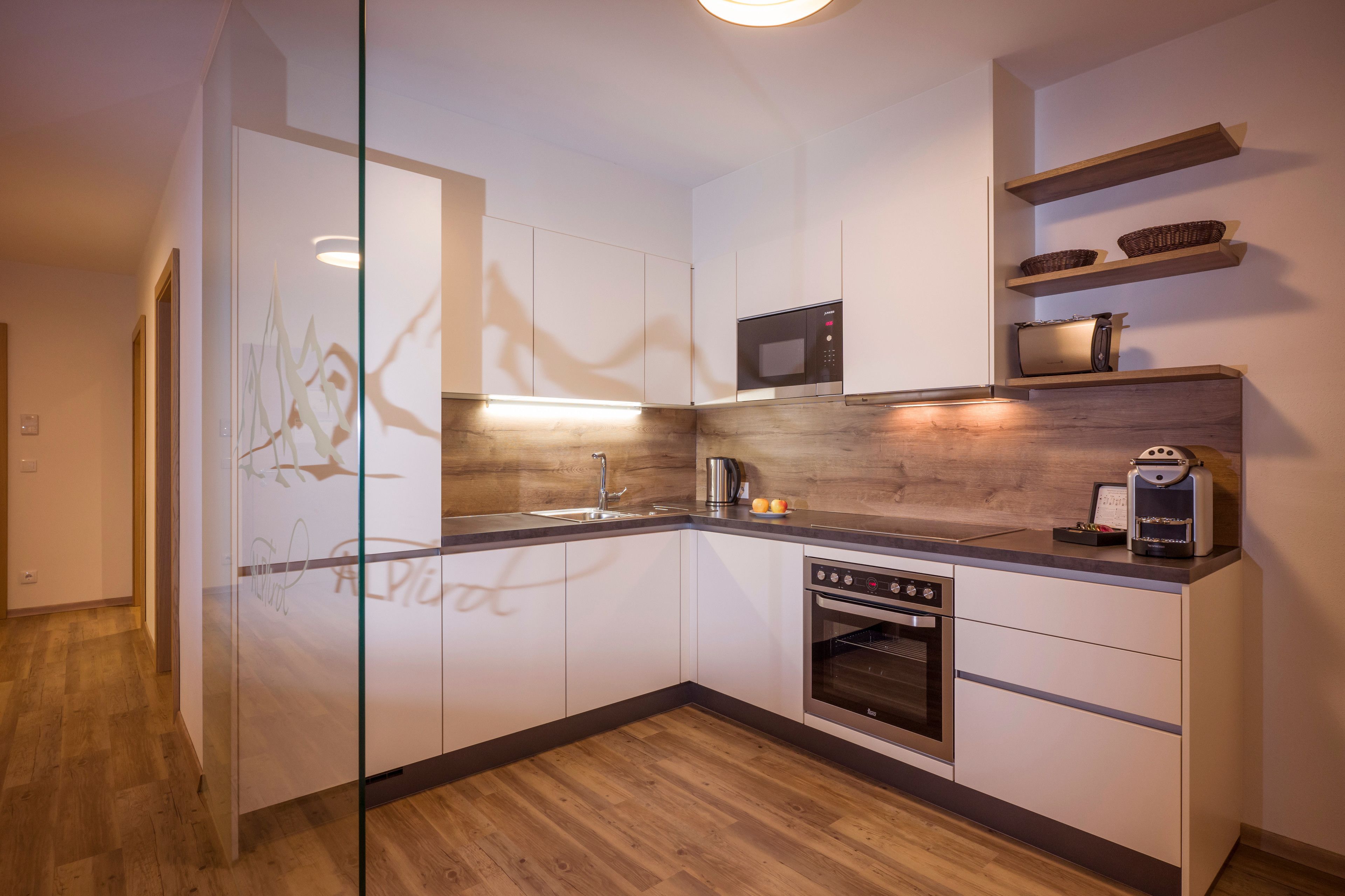 Una cocina moderna con armarios blancos, microondas, cafetera y suelo de madera.