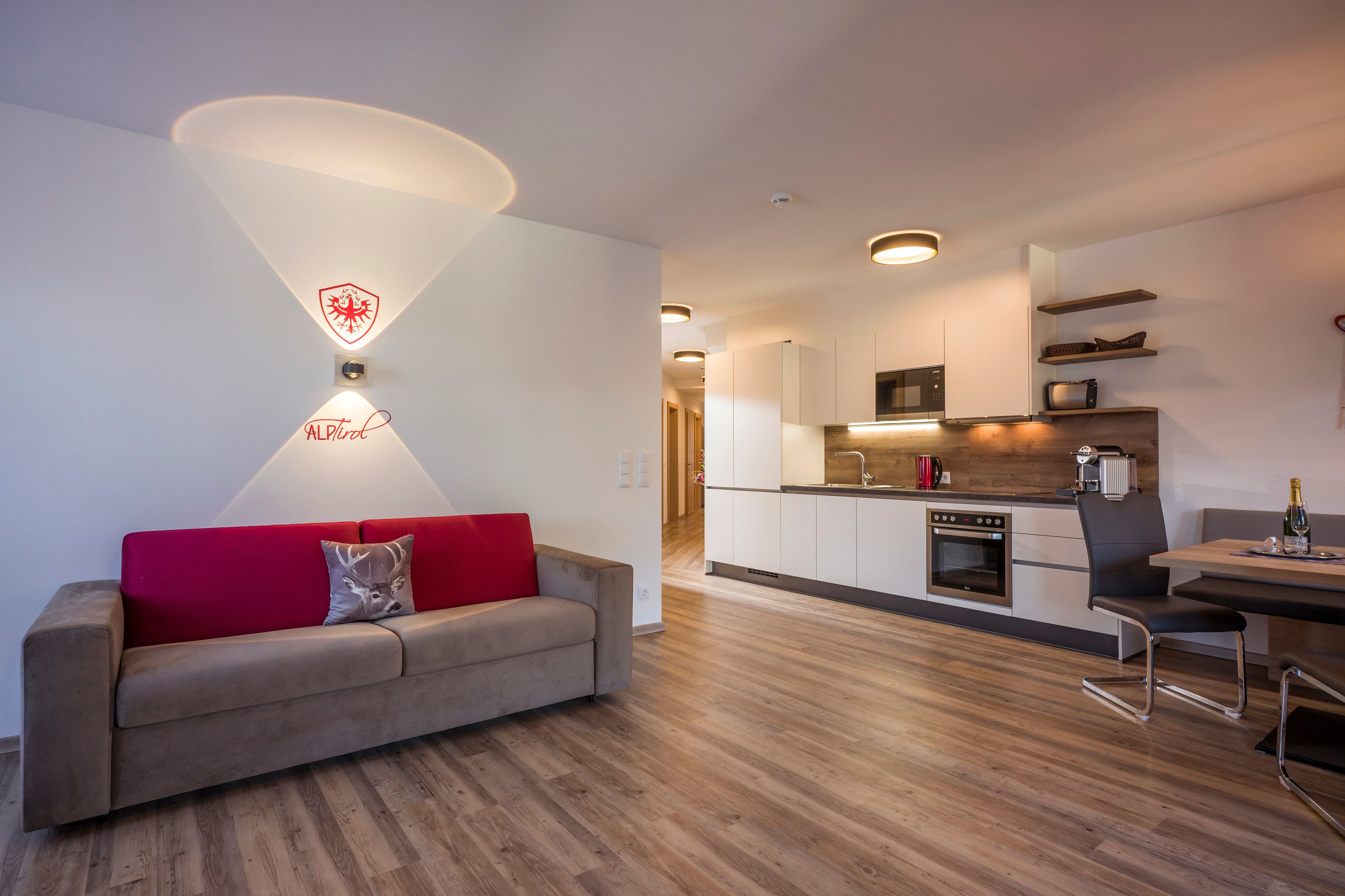 Una sala de estar moderna con un sofá rojo, una cocina con armarios blancos y un comedor con mesa y sillas.