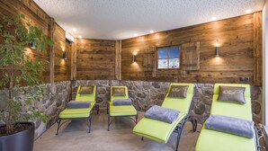 Un'area spa con pareti in legno, elementi decorativi in pietra e diversi lettini prendisole con cuscini.