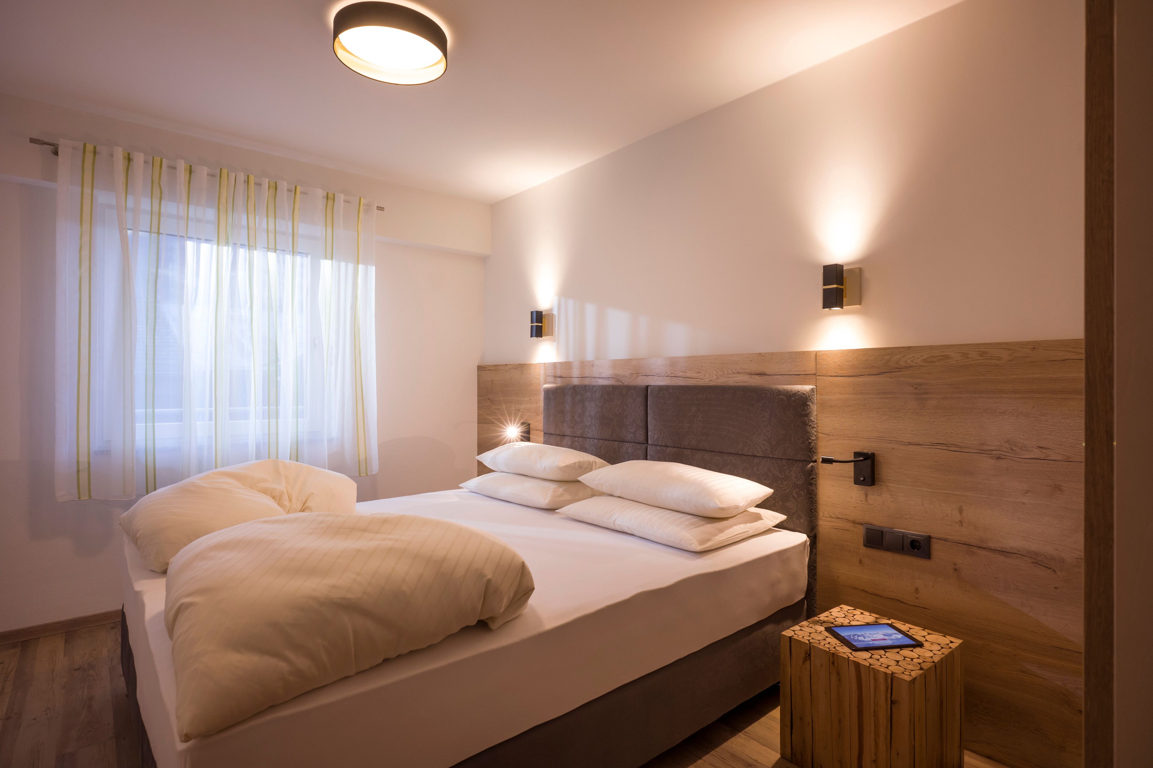 A modern bedroom with a large bed, bedside tables, and a nightstand with a tablet.