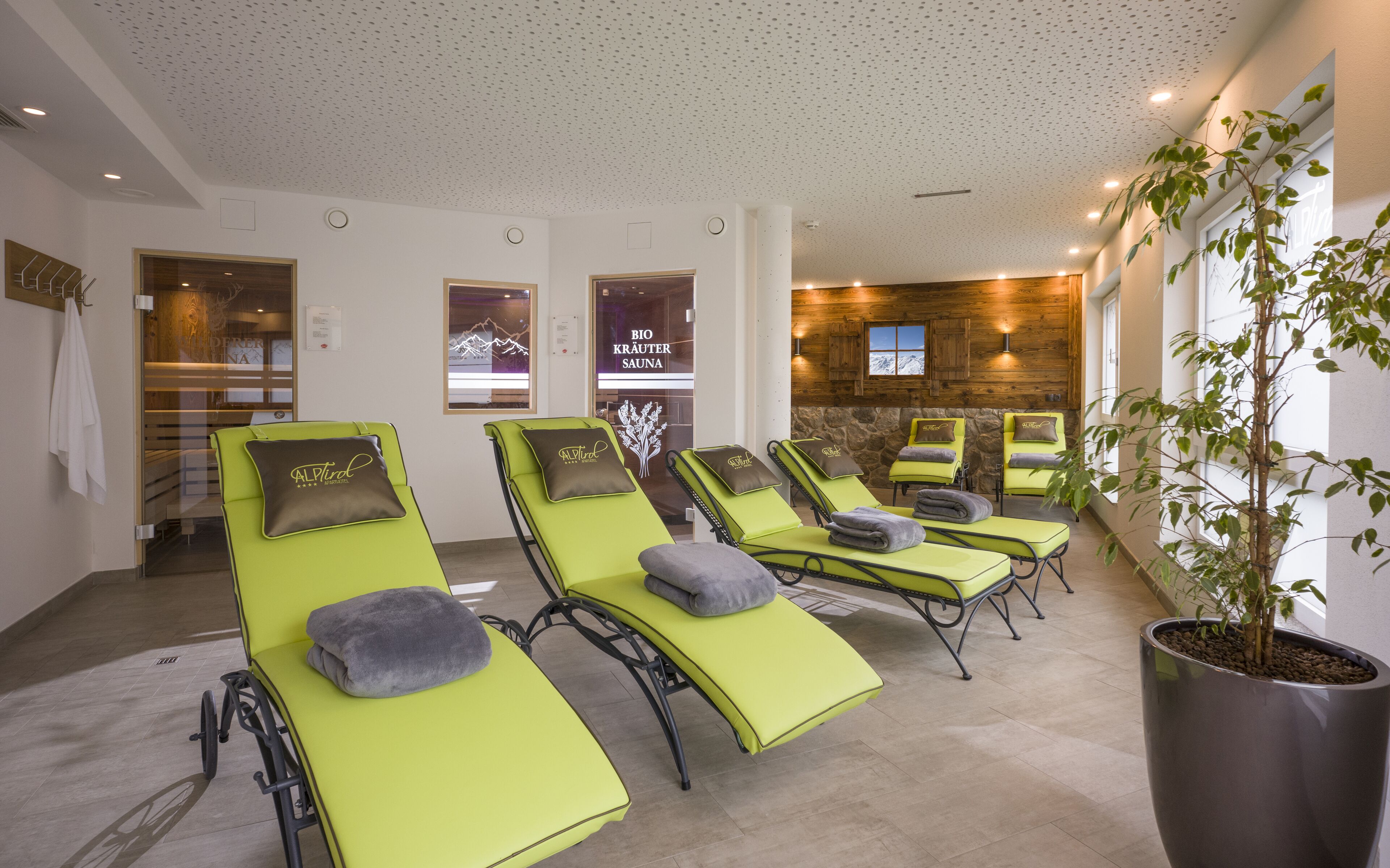 Ein Wellnessbereich mit grünen Liegen, einer Steinwand und einem Blumentopf.