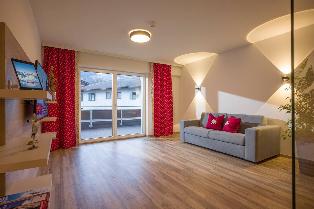 A modern living room with a grey sofa, red curtains, and a large window.
