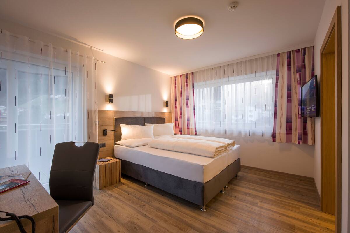 A modern hotel room with a bed, a desk, a chair, and a TV.