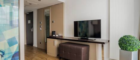 Une chambre d’hôtel moderne avec un plancher en bois, un téléviseur à écran plat, un banc en cuir marron et une plante en pot.