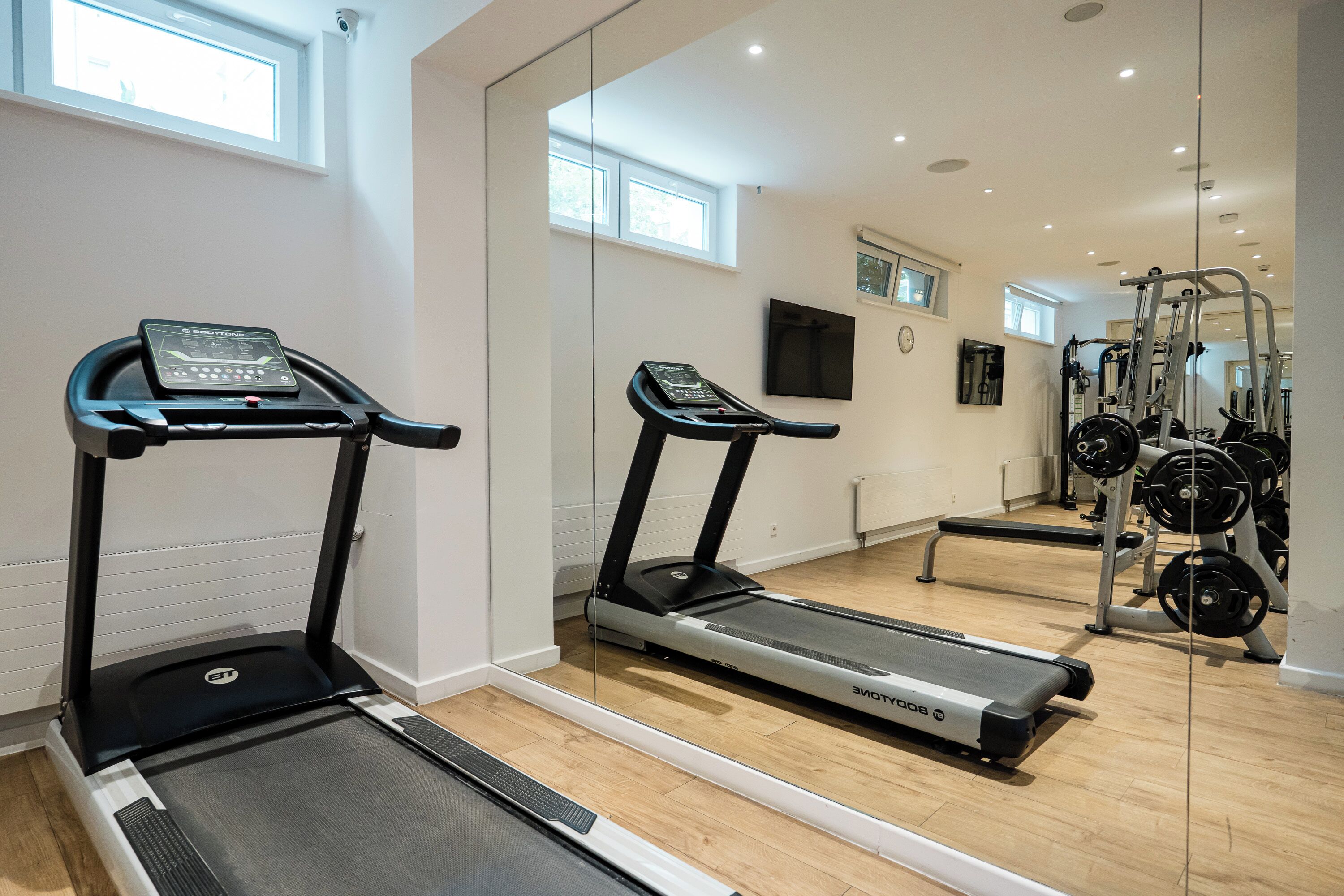 Un gimnasio con cintas de correr, una banca para pesas y un espejo que refleja los equipos.