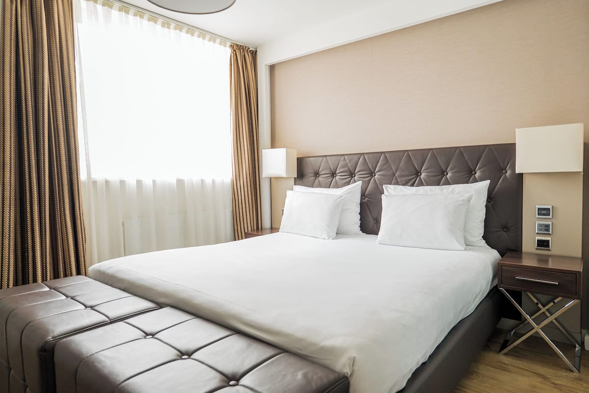 Een hotelkamer met een groot bed, een hoofdeinde, twee bedlampjes en een nachtkastje met een lamp.