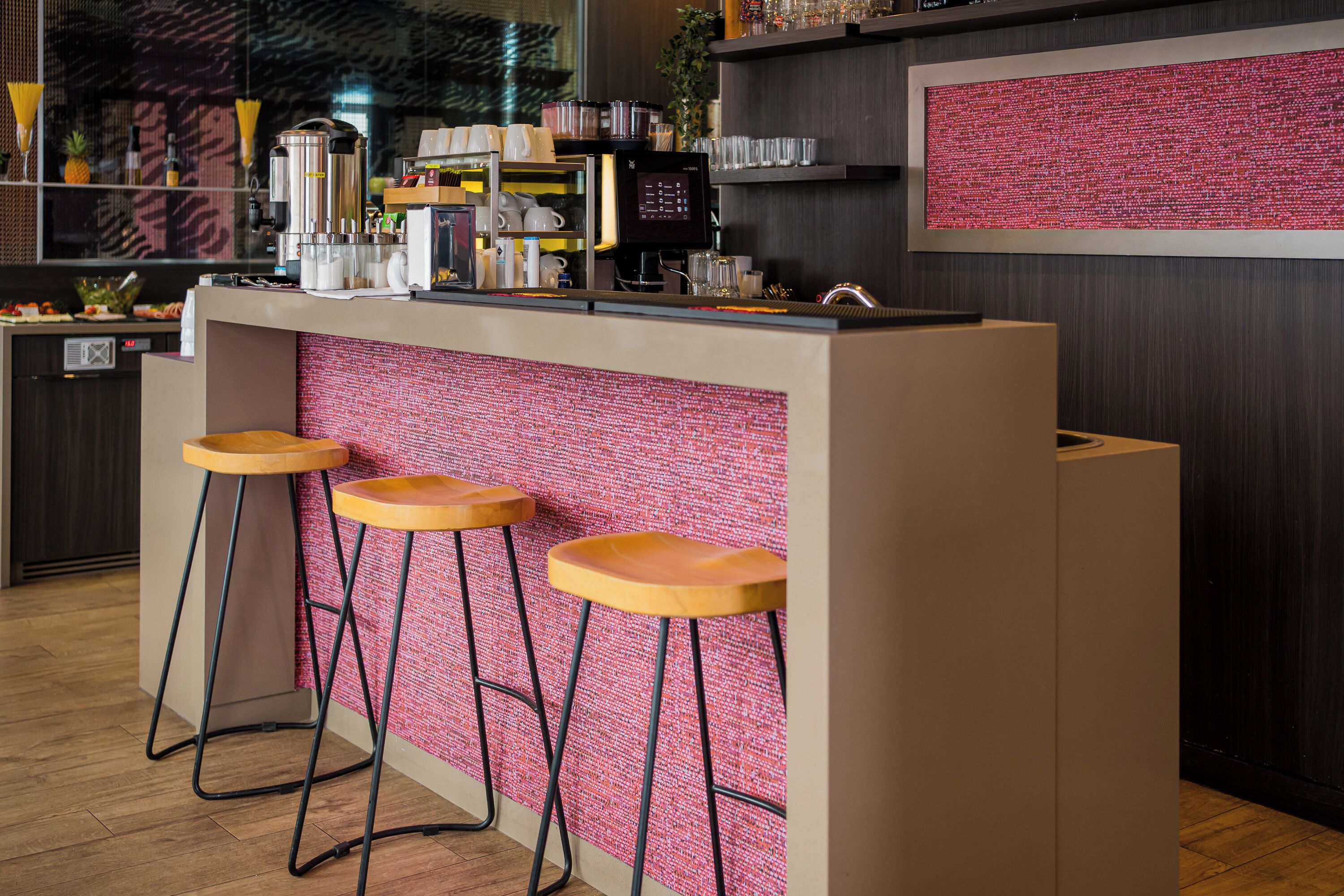 A bar area with stools, a coffee machine, and shelves with glasses and cups.