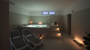 A spa room with a hot tub, two lounge chairs, and candles providing ambient lighting.