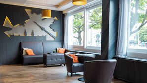 A modern hotel lobby with a dark-colored sofa, a round table, and a large window offering a view of the city.