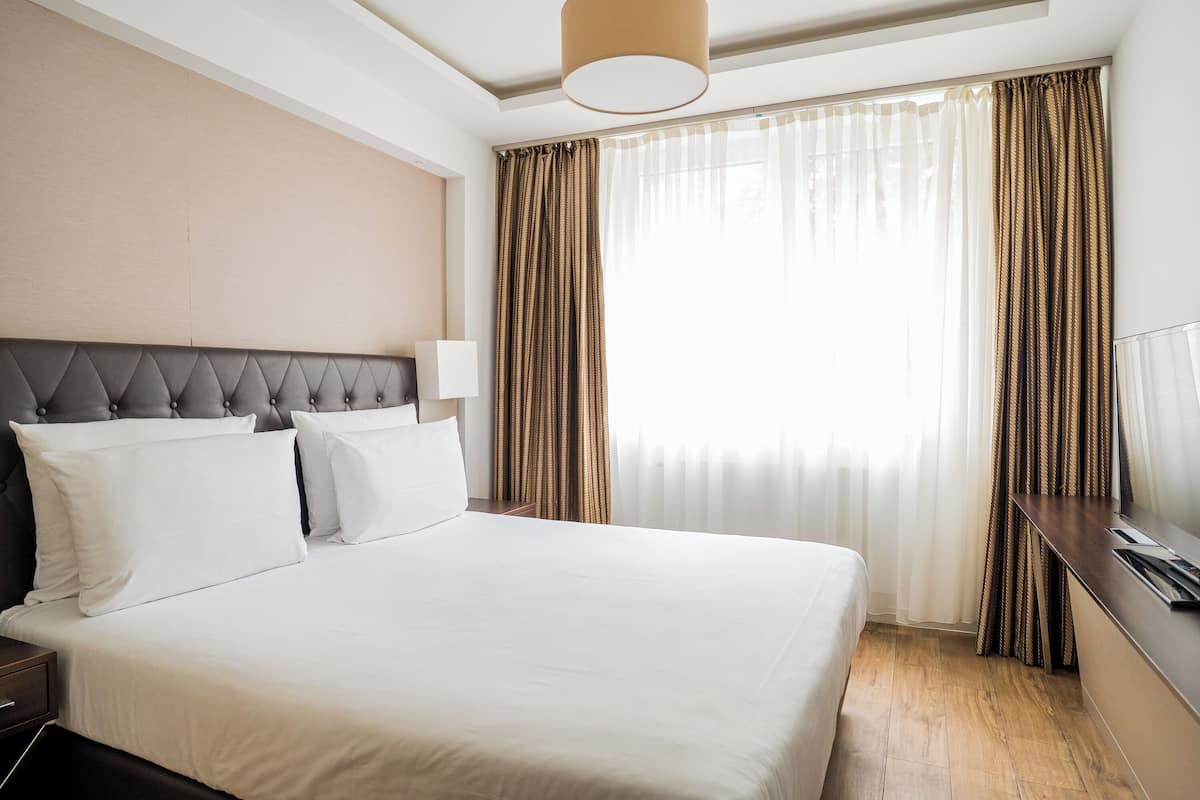Een hotelkamer met een groot bed, een hoofdeinde, een nachtkastje en een raam met gordijnen.