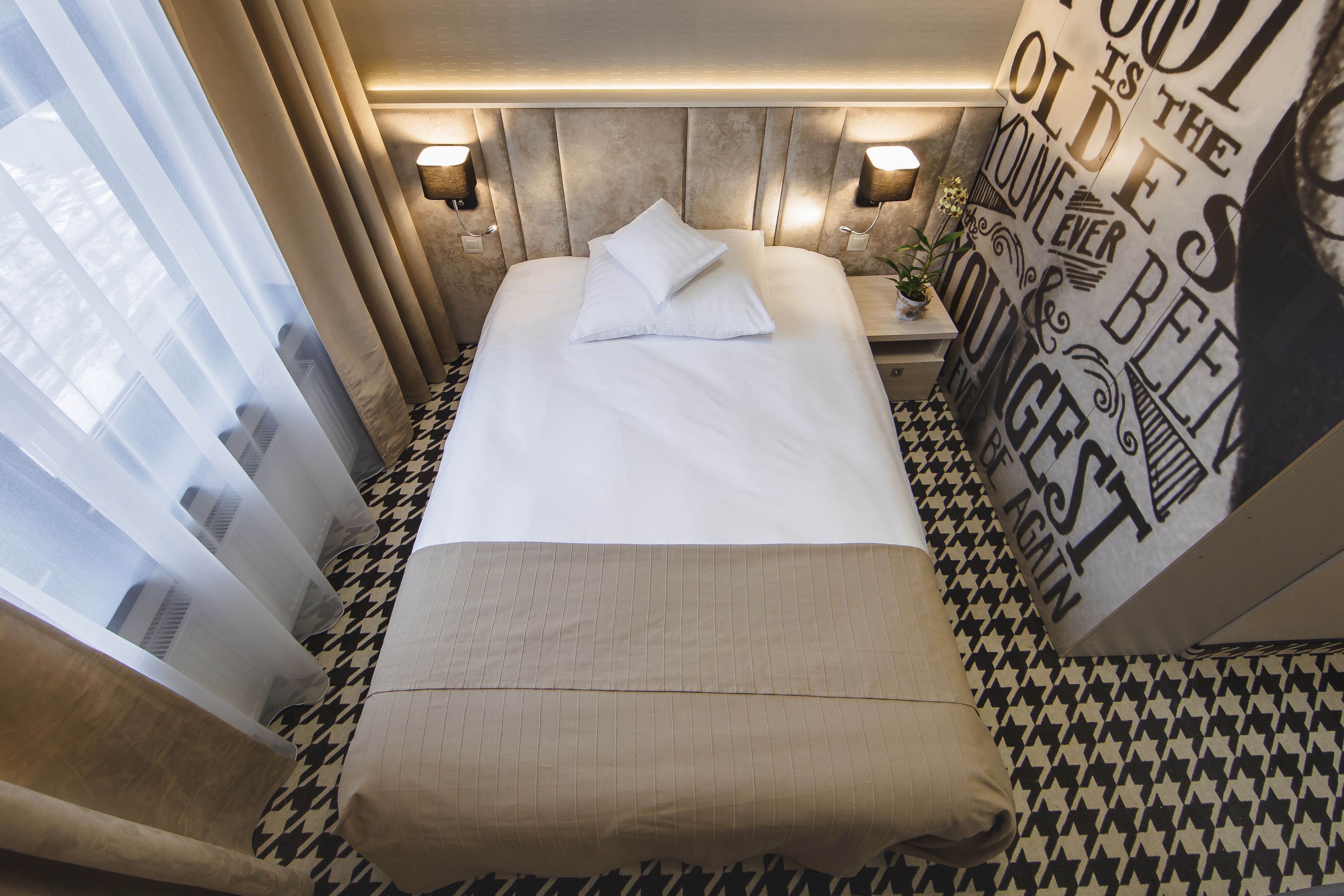 Una habitación de hotel con una cama bien hecha, piso estampado y una pared con texto motivacional.