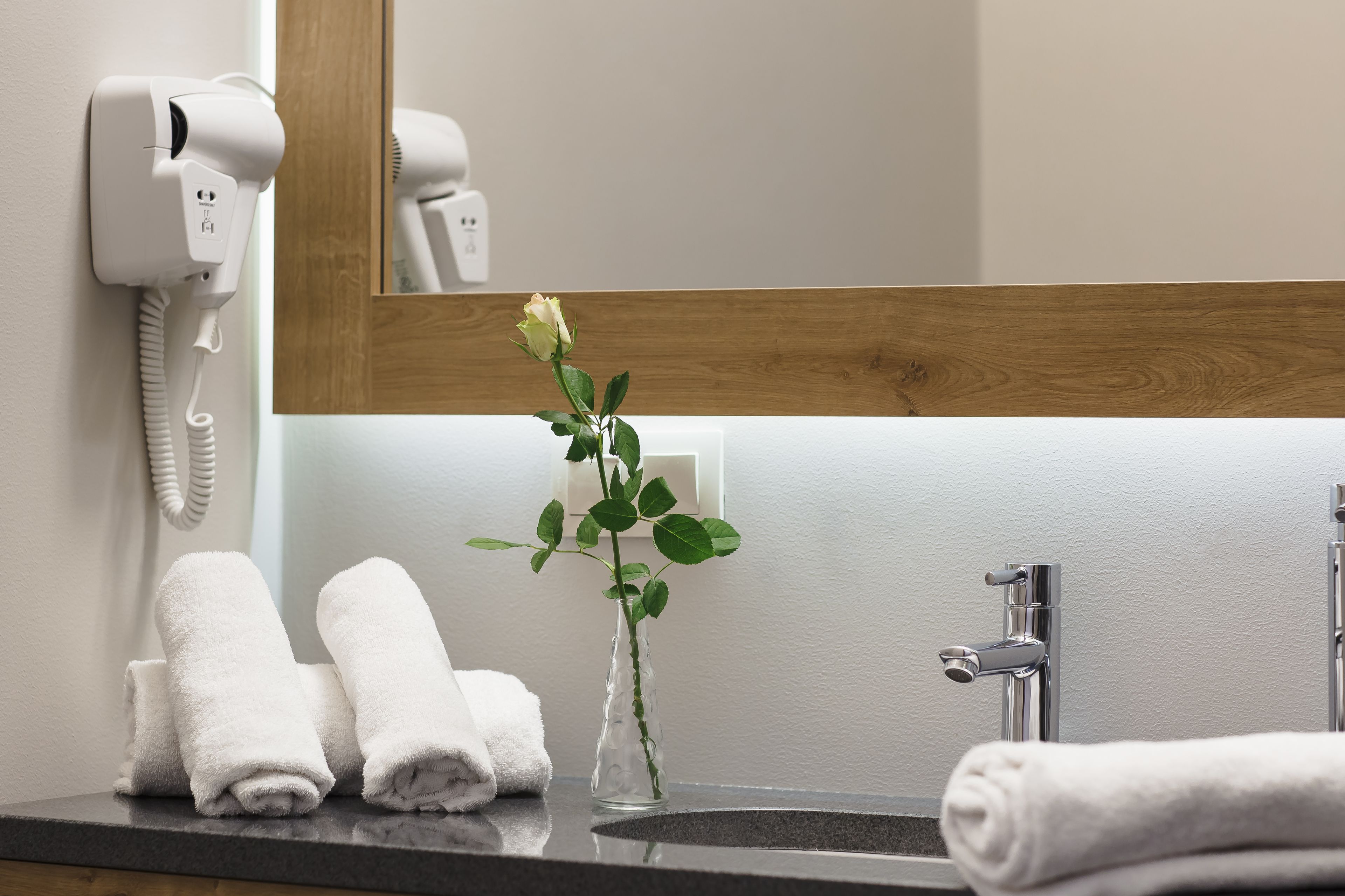 A bathroom with a hairdryer, a vase with a plant, and neatly folded towels.