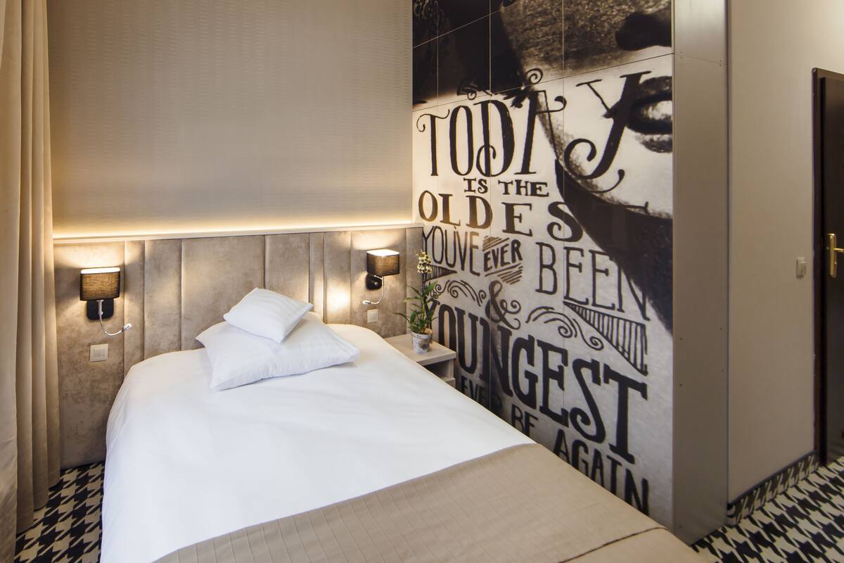 Una habitación de hotel con una cama, una pared con una cita motivacional y dos lámparas fijadas a la pared.