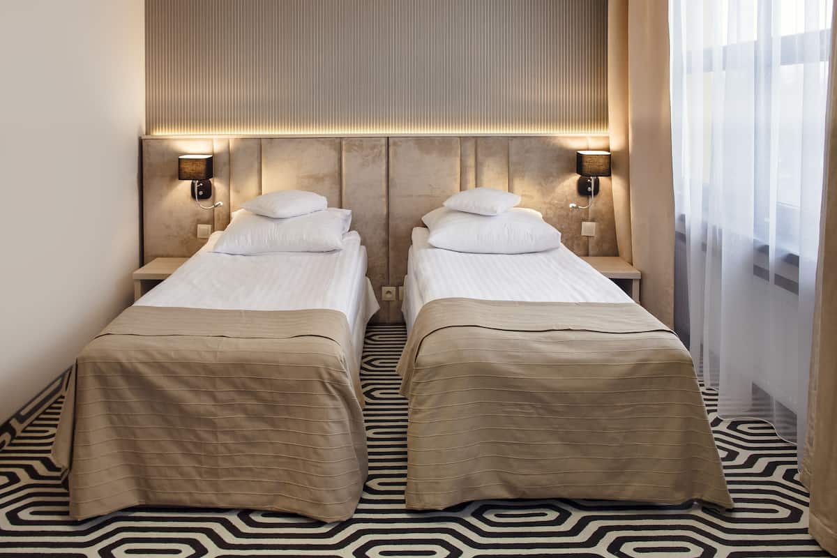 Una habitación de hotel con dos camas, piso estampado y cabecera con iluminación integrada.