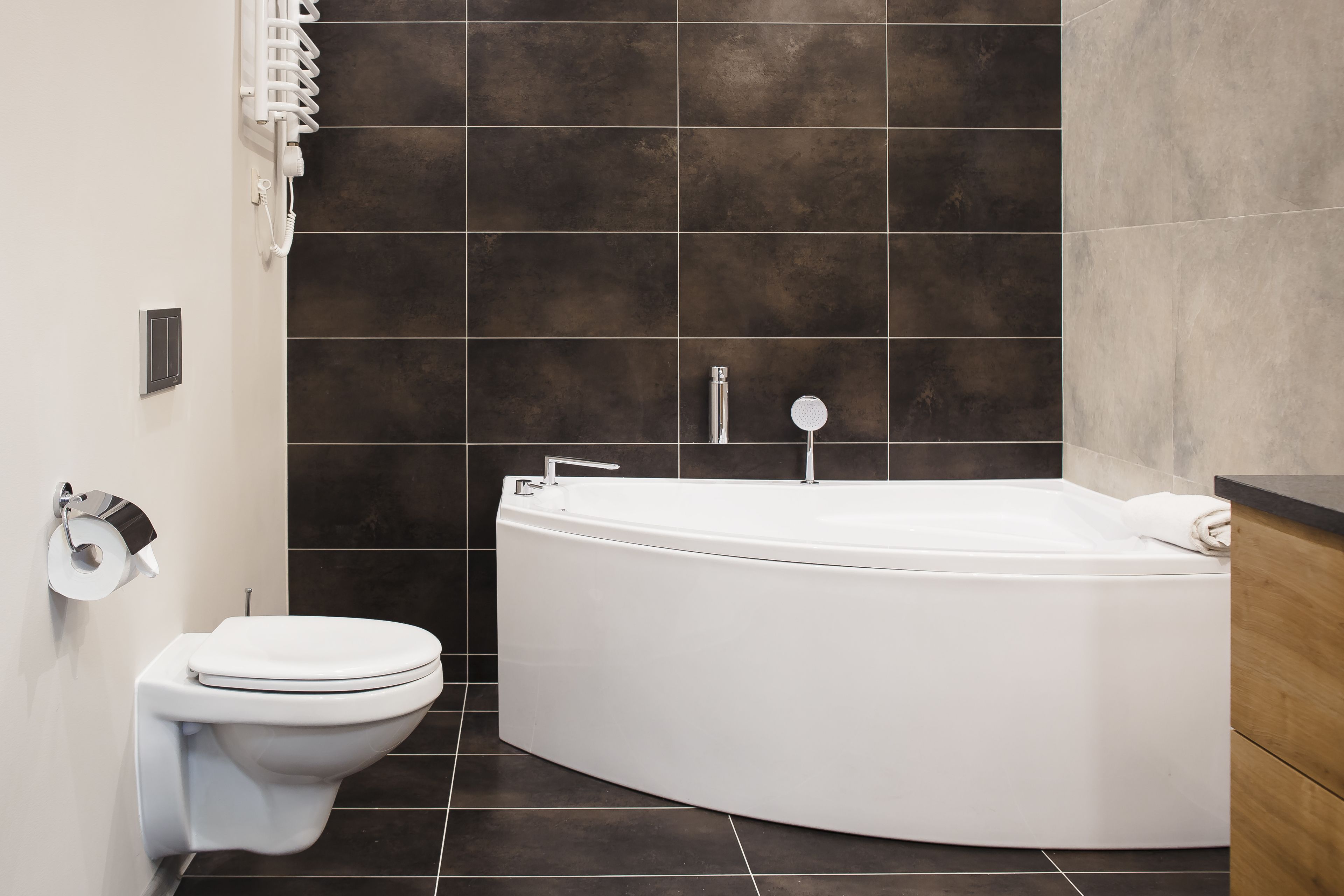 Un baño moderno con inodoro blanco, bañera y paredes de baldosas oscuras.