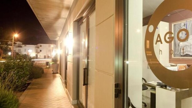 A hotel entrance with a glass door featuring a circular logo and a view of the interior. - Agorà Hotel (Calamandrana)