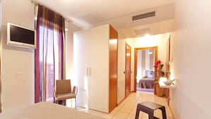 A hotel room with a bed, a chair, a desk, a TV, and a bathroom visible through an open door. - Agorà Hotel (Calamandrana)