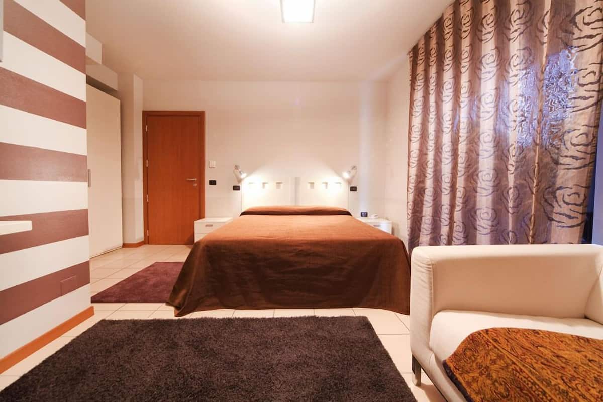 Hotellihuone, jossa on sänky, yöpöytä, tuoli ja verhot.