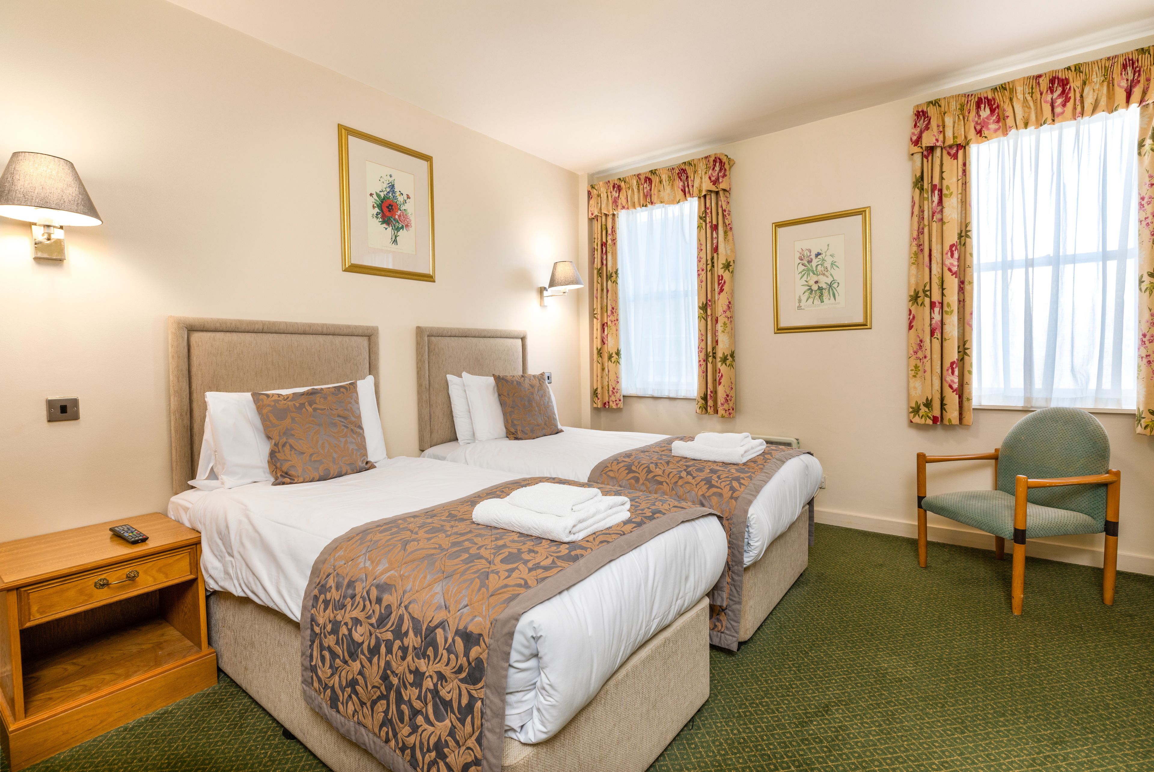 A hotel room with two beds, a nightstand, a chair, and two wall-mounted lamps.