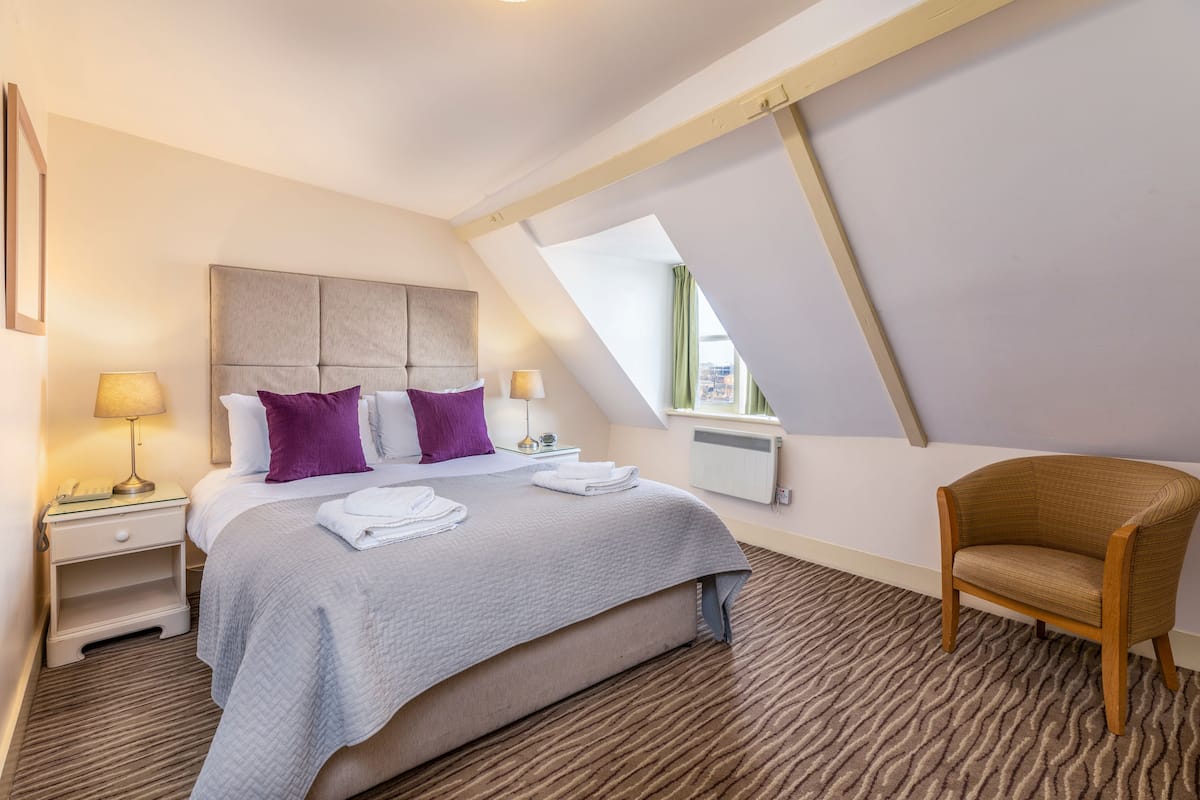 Ein Hotelzimmer mit Bett, Nachttischen, einem Sessel und einem Fenster.