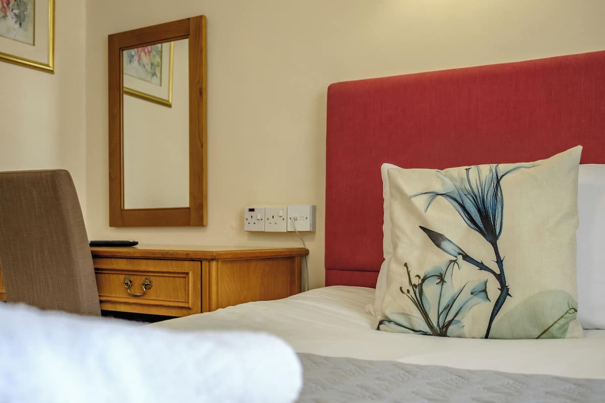 Ein Hotelzimmer mit einem Bett, einem Nachttisch aus Holz, einem Spiegel und einem roten Kopfteil.