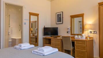 A hotel room with a bed, a desk, a television, a mirror, and a bathroom.