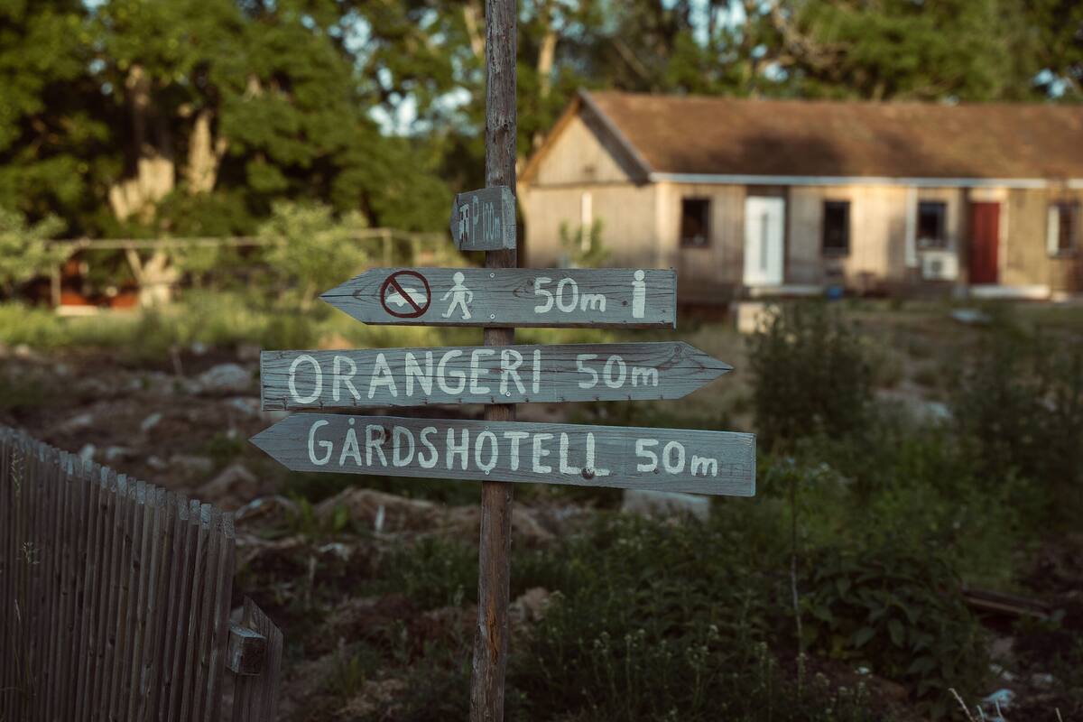 A wooden signpost with directional arrows pointing to Orangeri and Gardshotell, both 50 meters away.