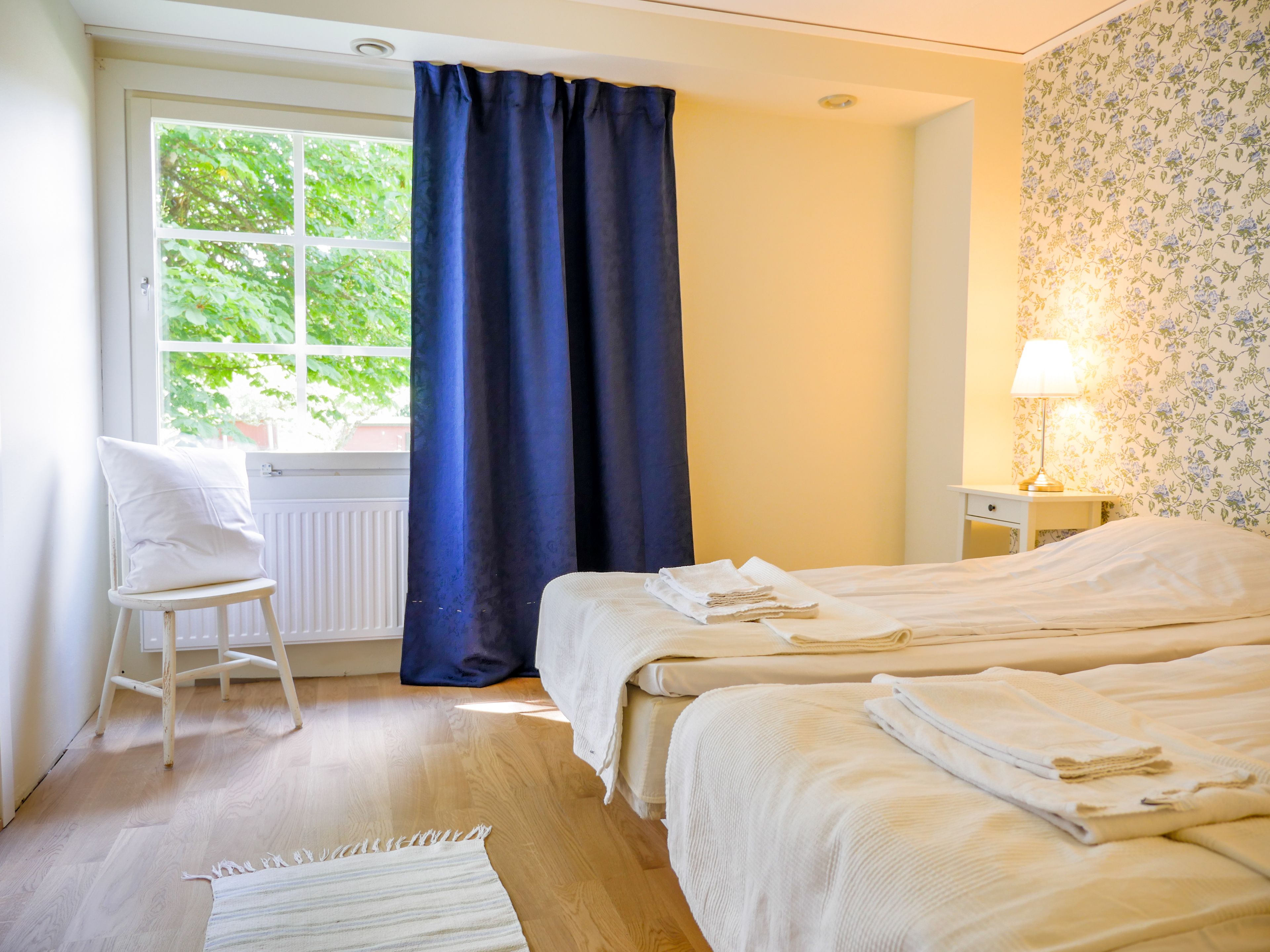 A room with a bed, a chair, a window with curtains, a lamp, and a radiator.