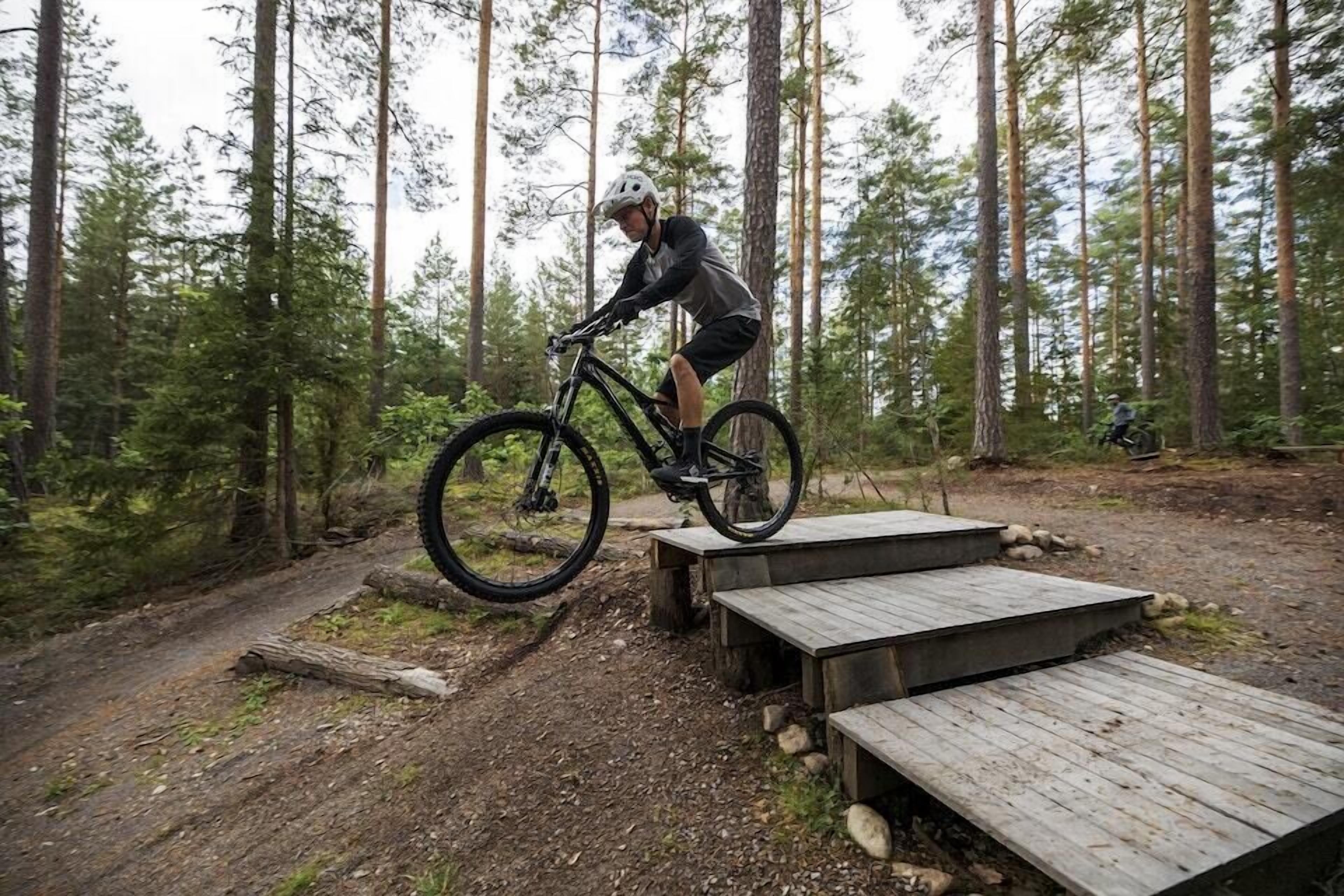 En mountainbikecyklist på en träplattform i ett skogsområde.