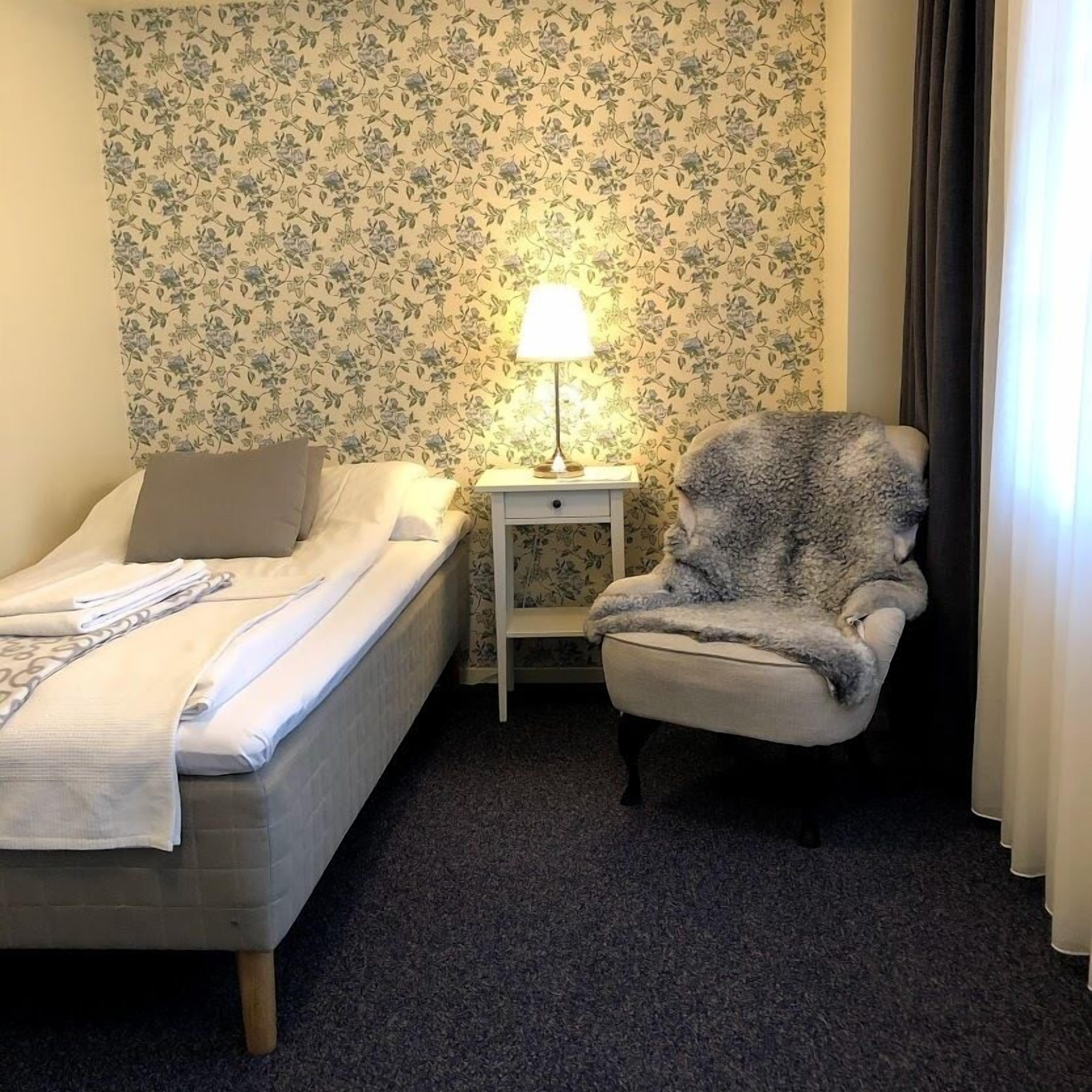 Una habitación de hotel con una cama, una silla, una mesita de noche y una lámpara.