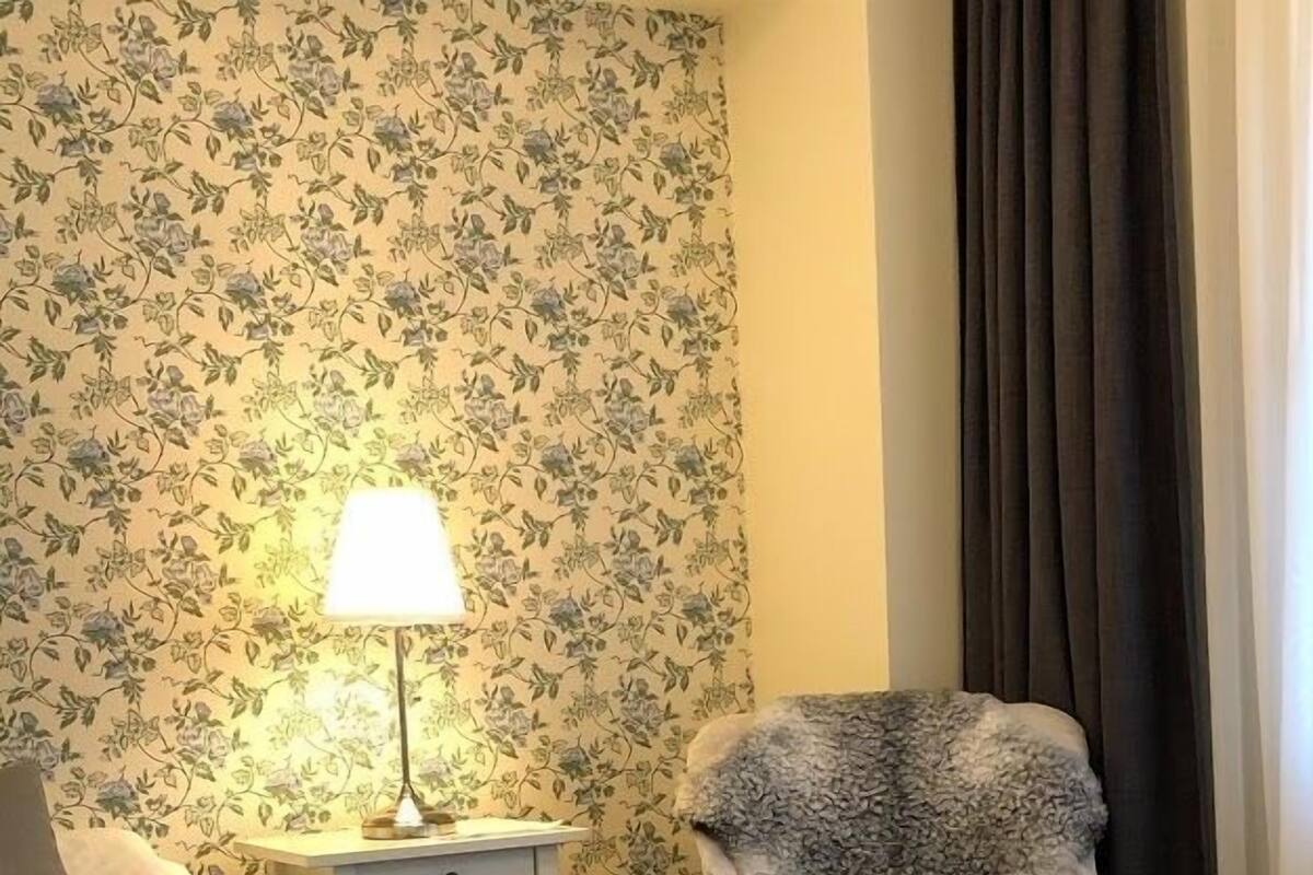 A hotel room with a bed, a chair, a nightstand, and a lamp.