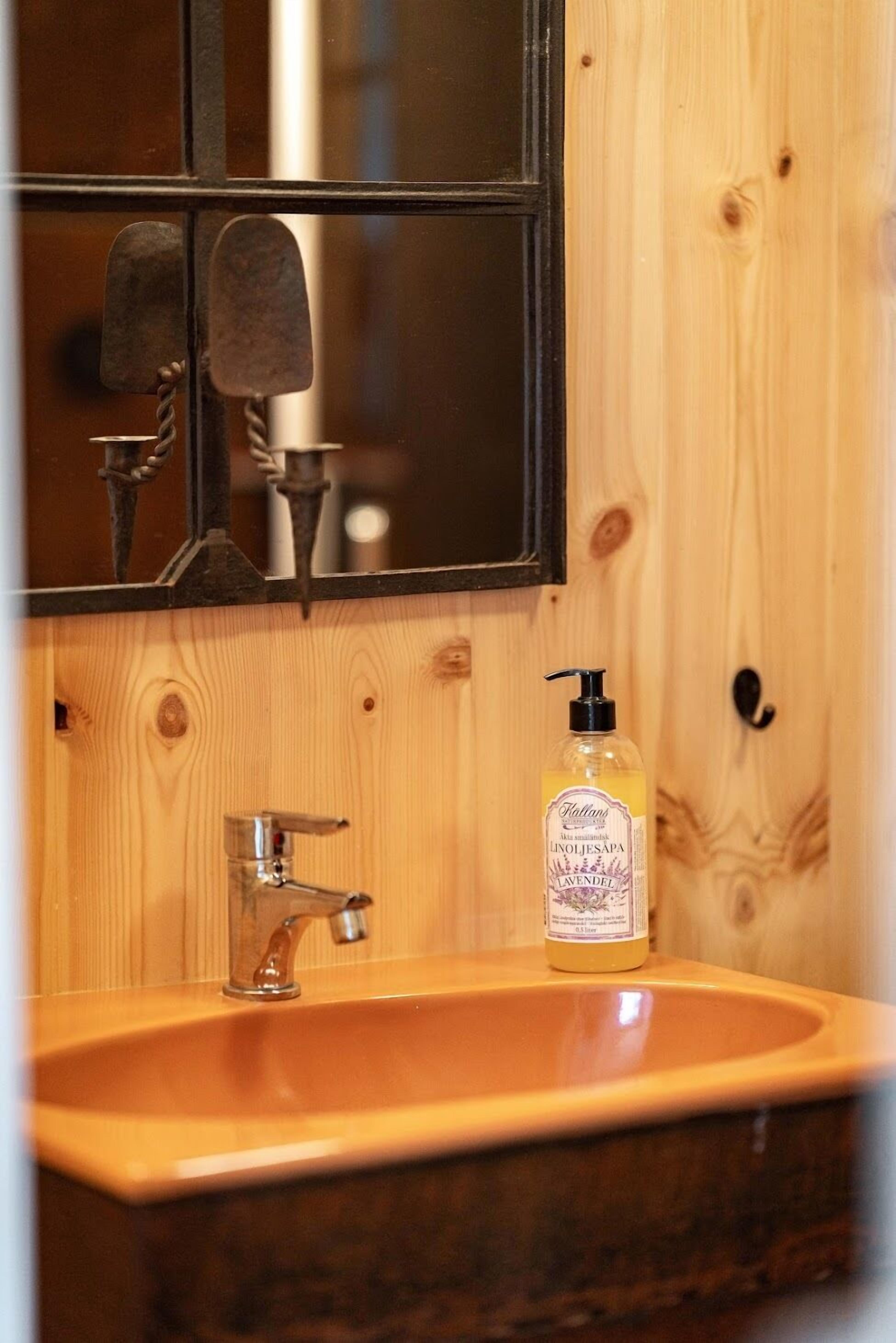 A wooden wall with a mirror, a sink, and a bottle of soap.