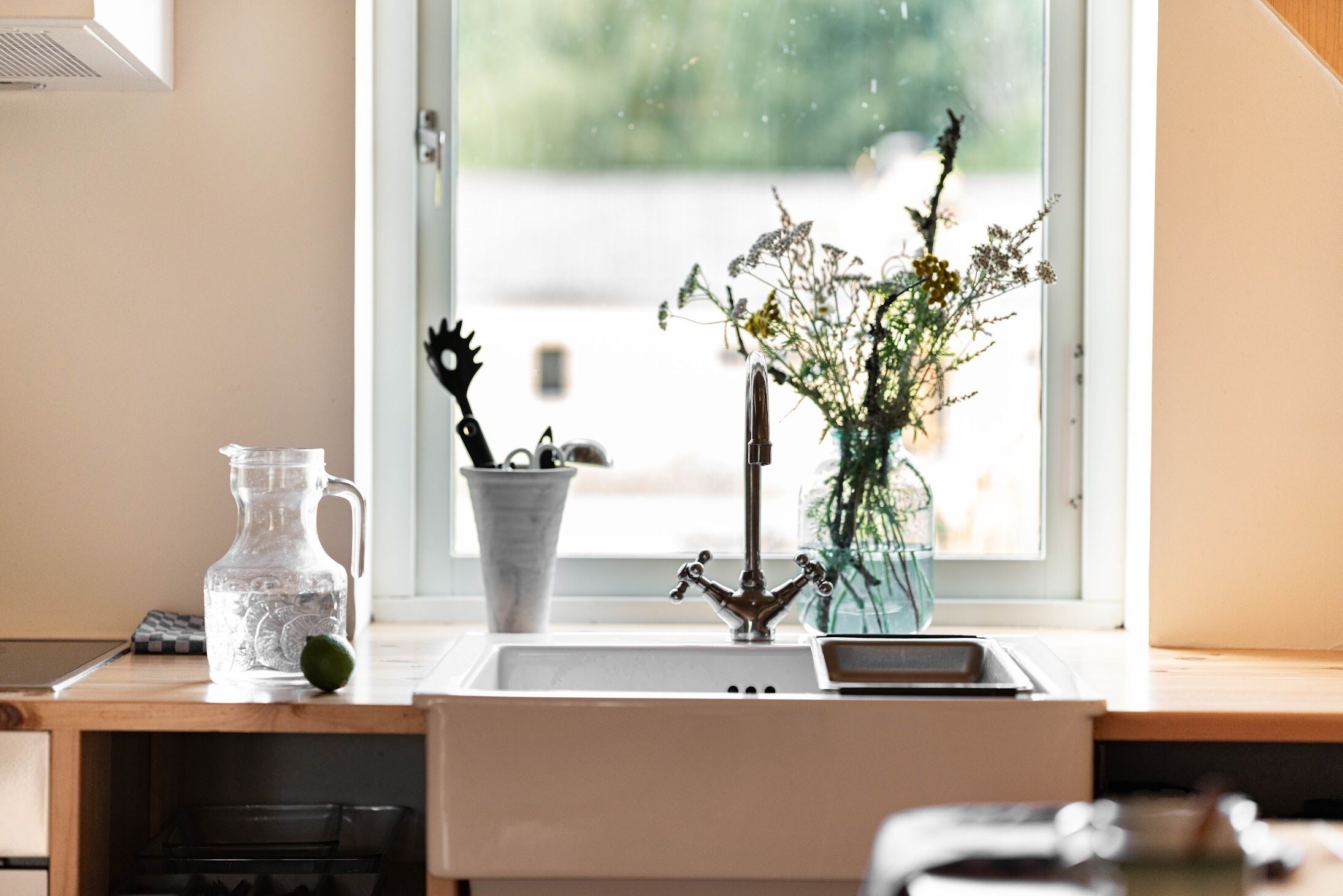 A kitchen with a sink, a vase with flowers, and a pitcher on the counter.