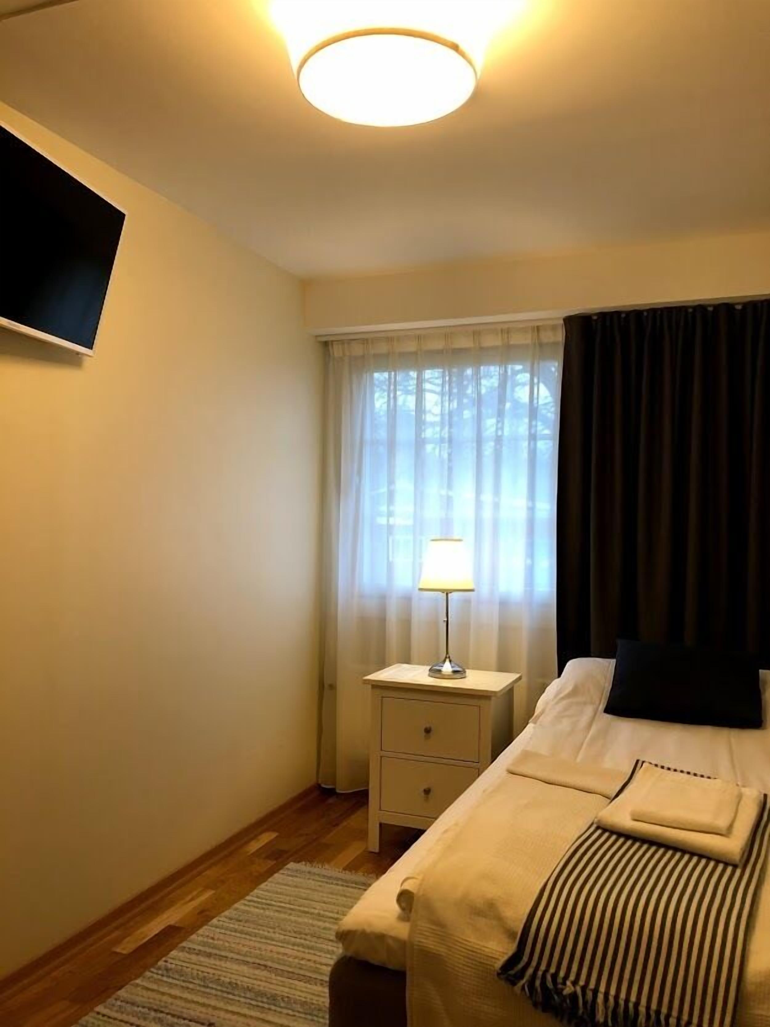 A hotel room with a bed, bedside table, lamp, and a window with curtains.