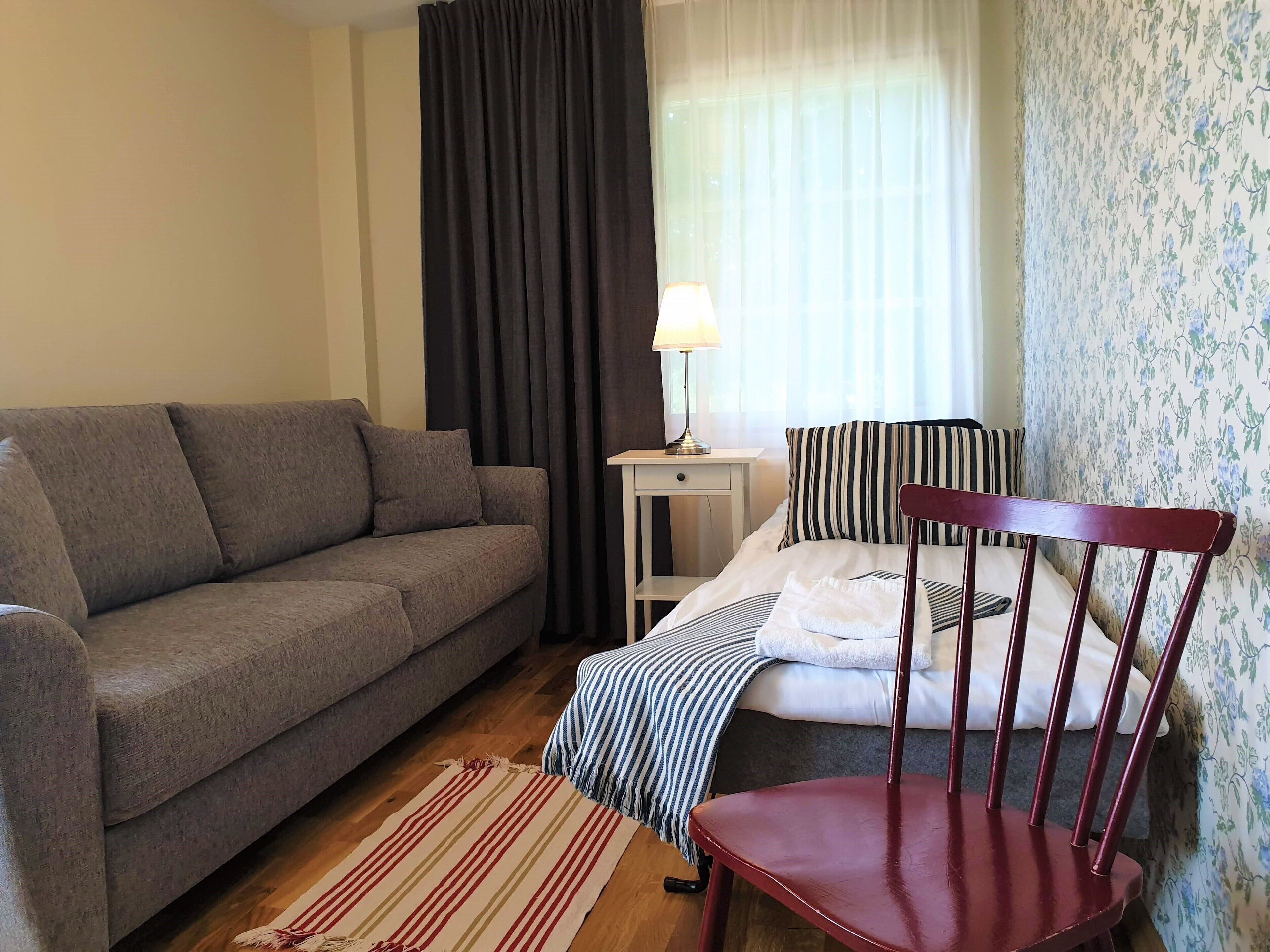 Una habitación con un sofá gris, una silla de madera, una manta a rayas y una lámpara sobre una mesita.