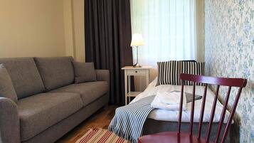 Una habitación con un sofá gris, una silla de madera, una manta a rayas y una lámpara sobre una mesita.