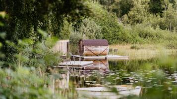 Una estructura de madera rústica con techo de metal, posiblemente un cobertizo o depósito, ubicada sobre una plataforma flotante en una masa de agua tranquila rodeada de densa vegetación.