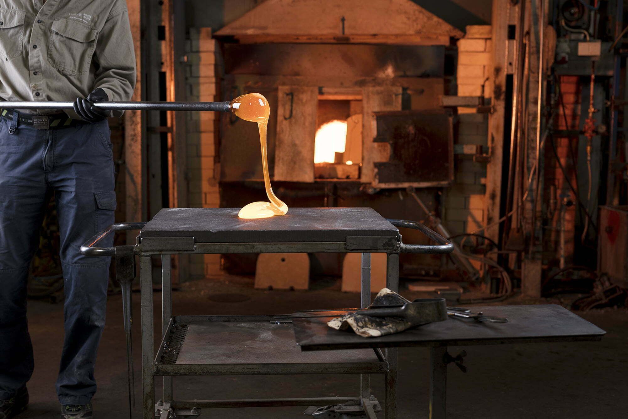 Una persona vertiendo metal fundido en un molde sobre una mesa metálica en un taller.