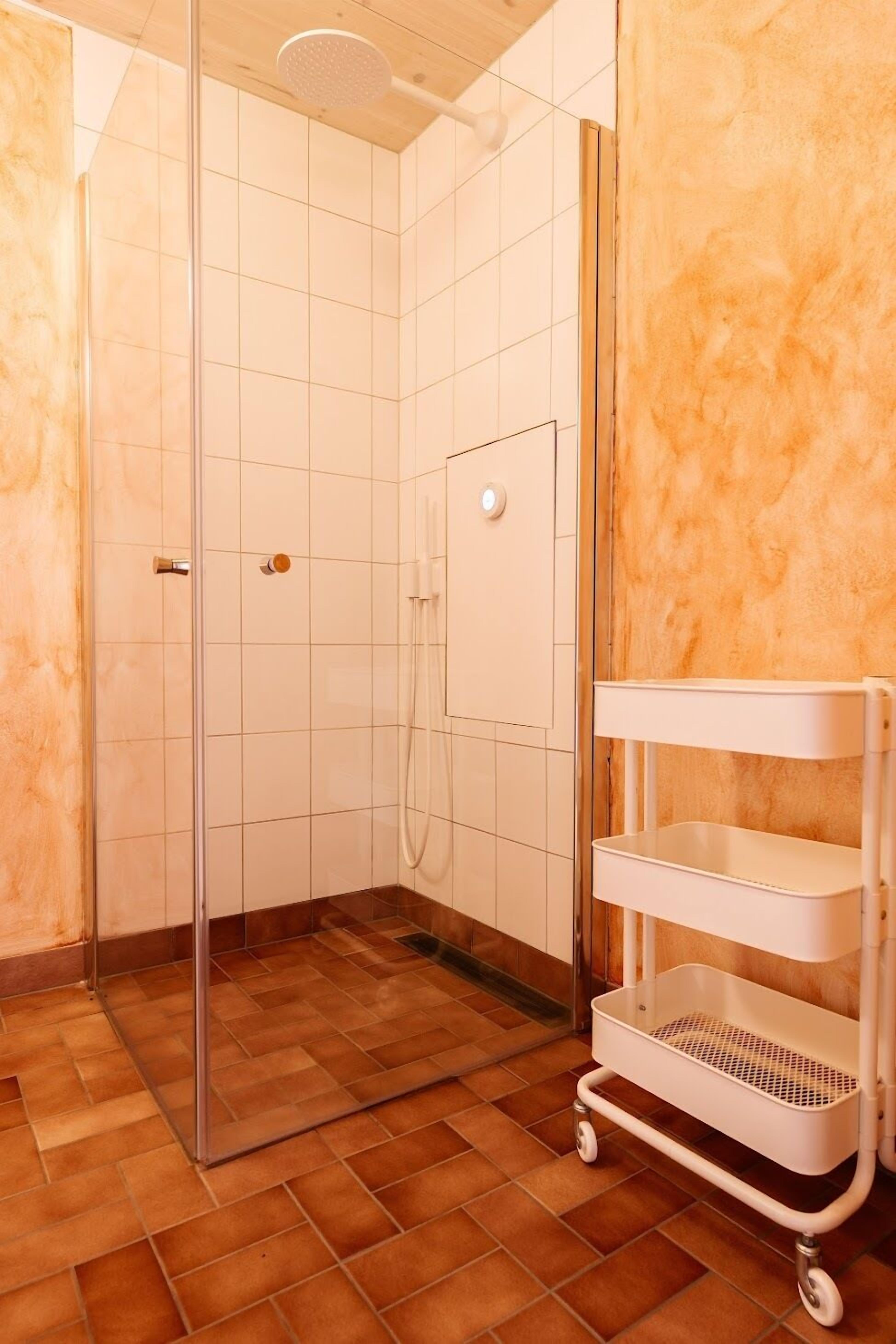 A shower area with a glass door, tiled walls, and a white shelf unit.