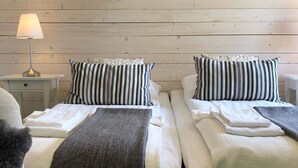 Ein Doppelzimmer mit zwei Betten, jeweils mit gestreiften Kissen und einer Decke, einem Nachttisch mit einer Lampe sowie einer Holzwand.