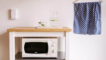 A kitchen area with a microwave on a white cart, a hanging rack with a blue and white checkered cloth, and a small table with a glass pitcher and glasses.