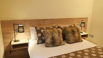 Una cama bien hecha con una colcha marrón estampada, dos almohadas mullidas y dos lámparas de noche sobre mesitas de madera.