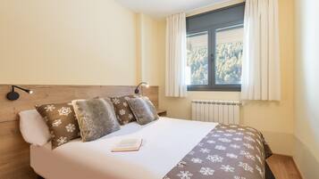 A neatly made bed with a patterned bedspread, a book on the bed, and a window with curtains.